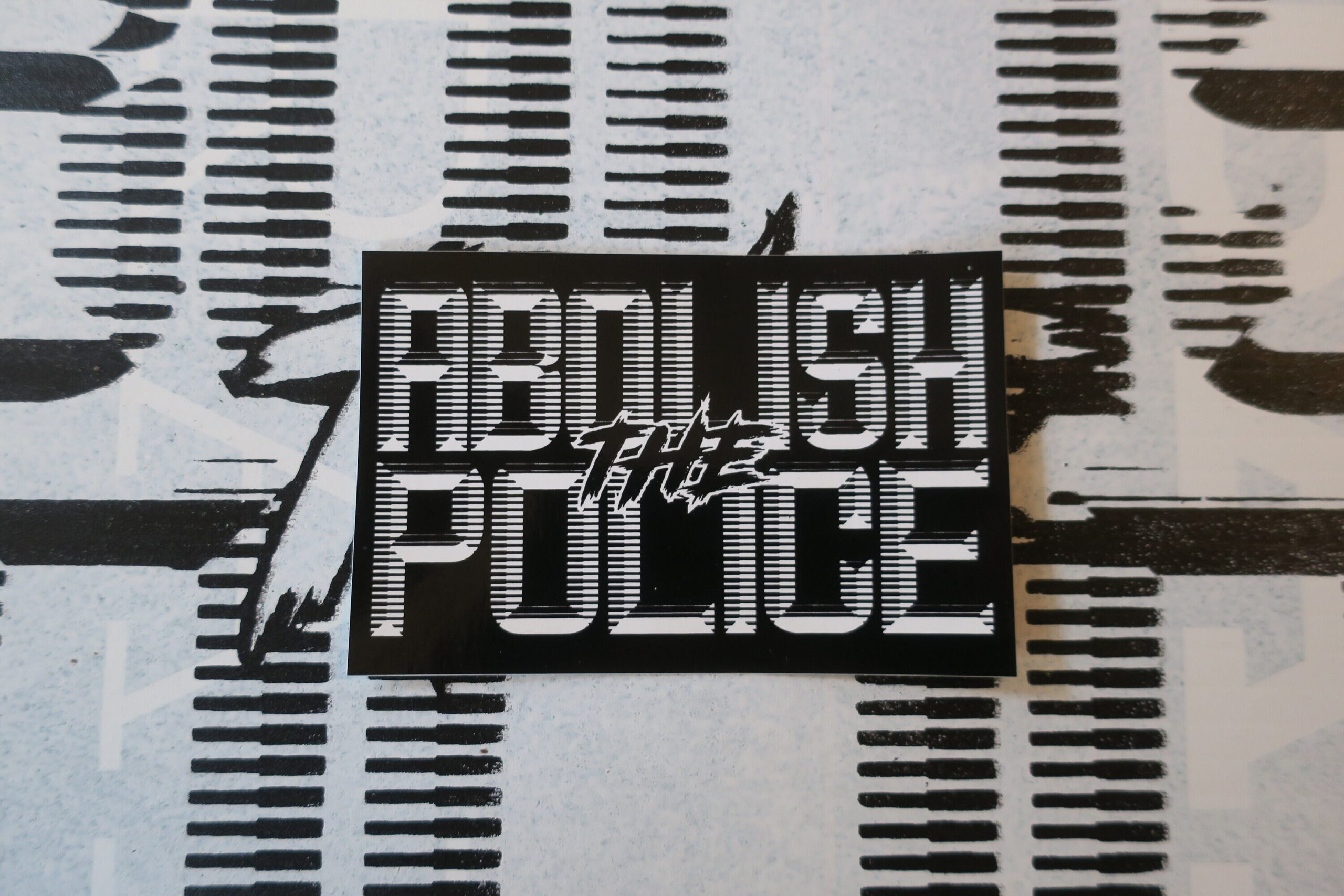 A background of a white sign with black retrofuturistic typeface reading "Abolish the Police." partially obscured by the cropped picture, upon which is a black sticker with white retrofuturistic typeface reading "Abolish the Police."