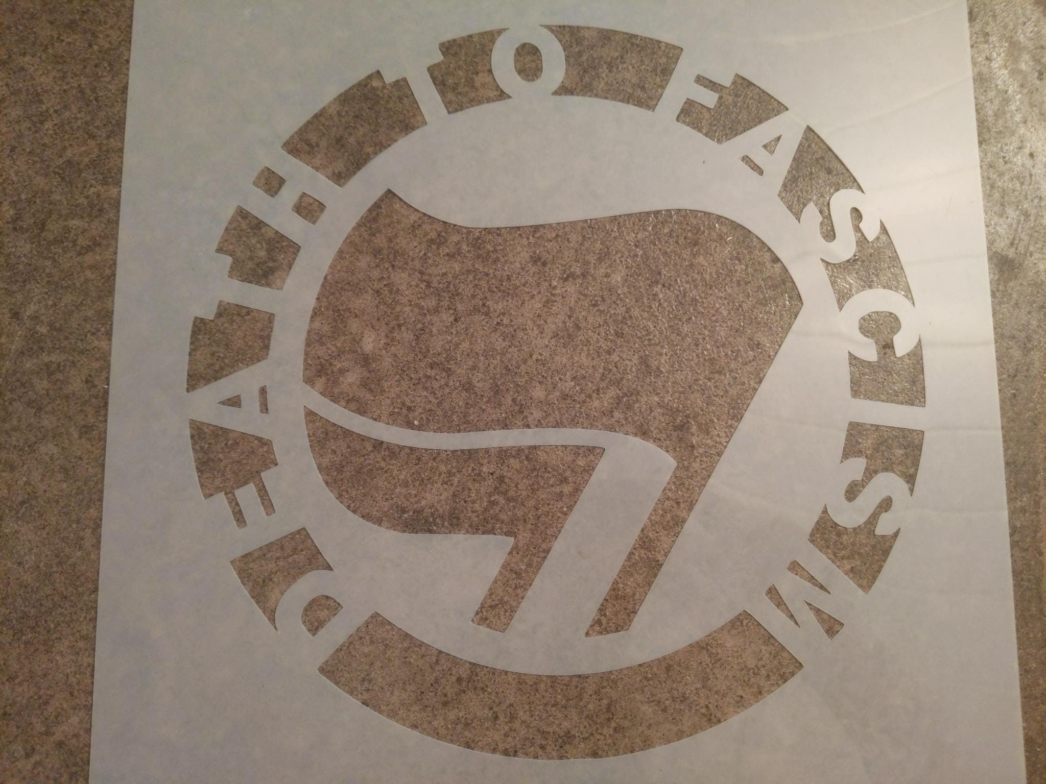 A translucent white mylar stencil reading "Death to Fascism" around the antifascist flags logo.