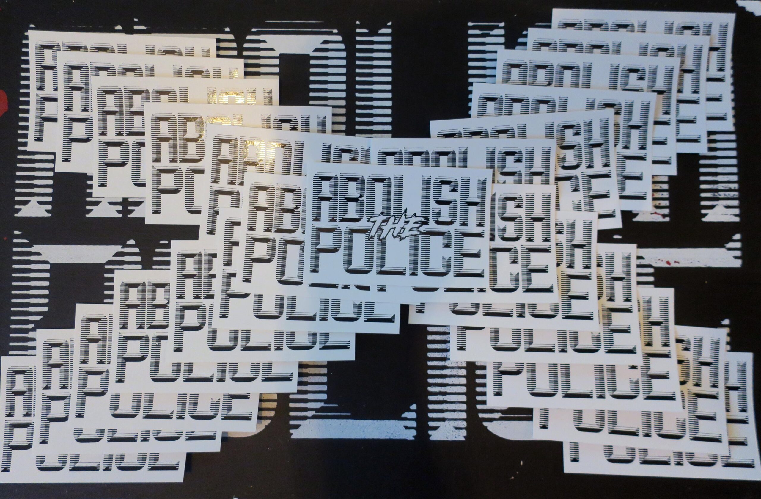 A background of a black sign with white retrofuturistic typeface reading "Abolish the Police." partially obscured by 20 white stickers arranged in an X with black retrofuturistic typeface reading "Abolish the Police."