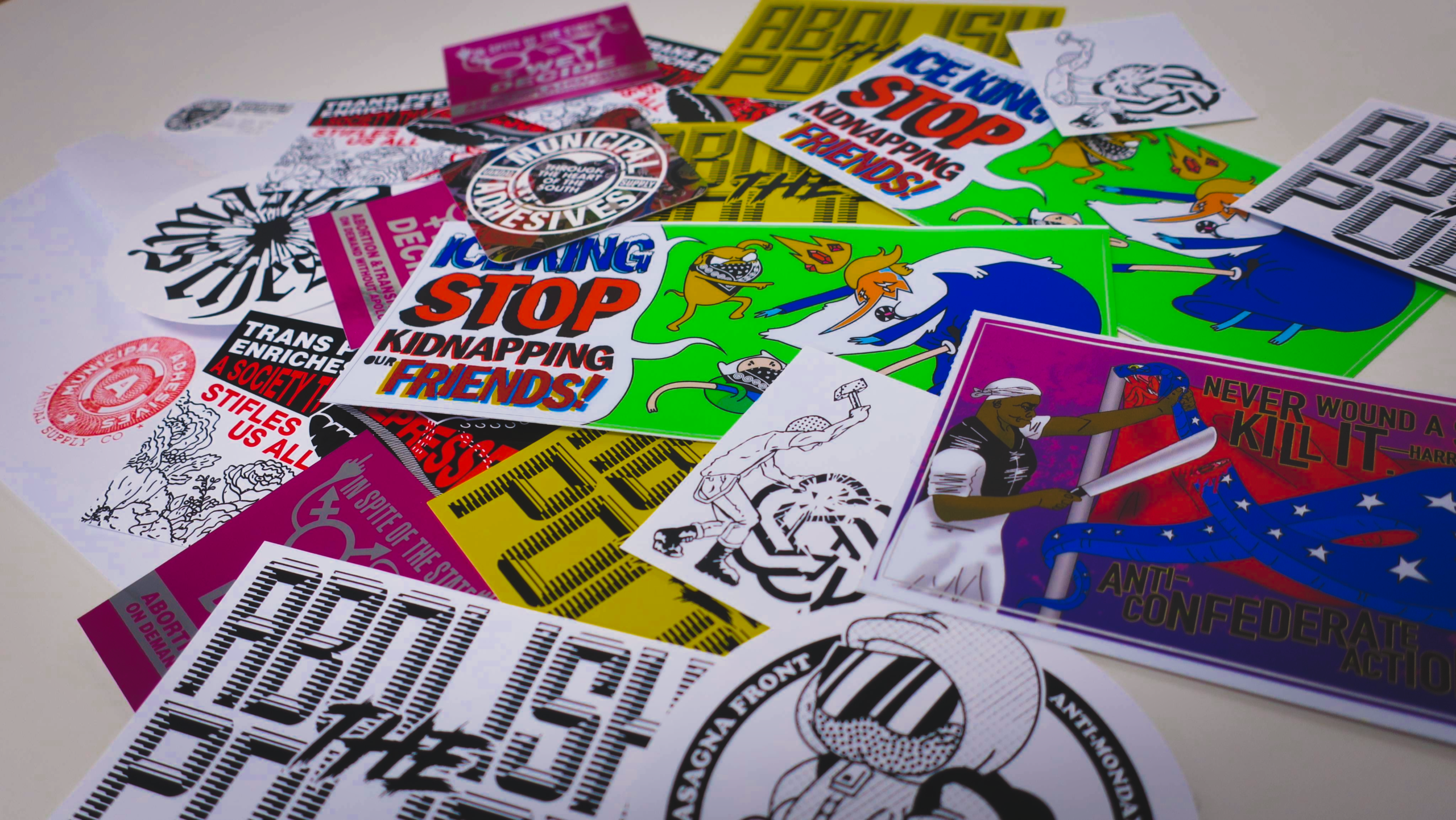 On a white smooth surface, a standard envelope dumps some 25 Municipal Adhesives stickers along with a business card.