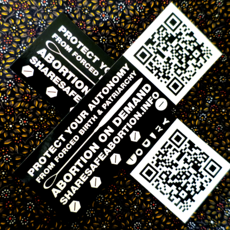 A floral background with two crossed black vinyl stickers. The sticker has a white Sims uterine suction curette across it and underneath a set of five white pills, four hexagonal and one round. Across the top of the stickers in white, the words "Protect Your Autonomy from Forced Birth & Patriarchy," and across the bottom in white, the words "Abortion on Demand," and separated by a line, the url "ShareSafeAbortion.info". To the left of this design on the stickers is a QR code that would point the scanner to the aforementioned URL.
