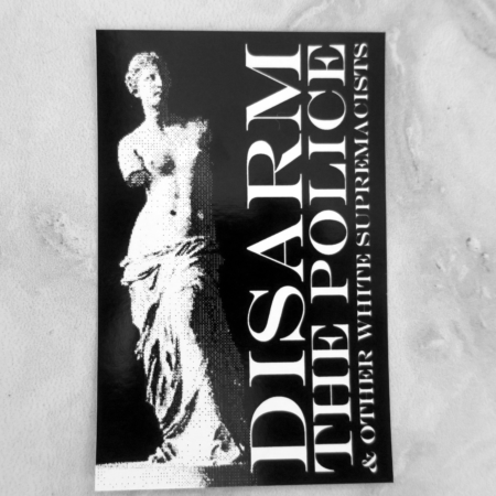 On a marbled surface, a black sticker with a white pixelated depiction of the Venus de Milo by sculptor Alexandros of Antioch. The words "Disarm the Police & Other White Supremacists" are tucked vertically facing upwards to the right of this statue in white.