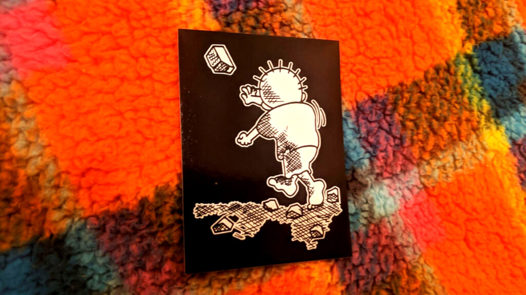 A sticker atop a fuzzy plaid background. The stickers show the refugee cartoon boy Handala, characteristically barefoot, throwing a rock at some unseen Israeli tank.