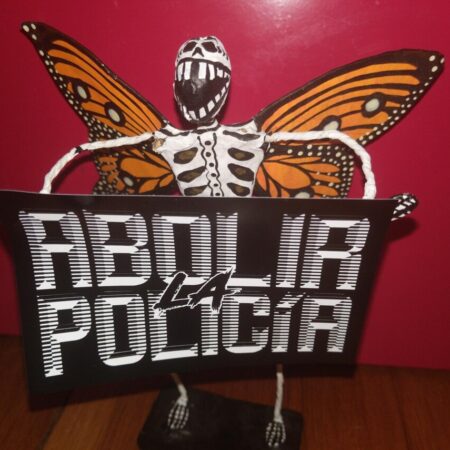 Un esqueleto con alas de mariposa sosteniendo una etiqueta que dice "Abolir la policía" en tipografía retrofuturista blanca sobre fondo negro.