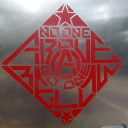 A closeup of a silver electrical box with a red spray painted stencil reading "No One Above, No One Below" around a circle-A anarchist symbol.