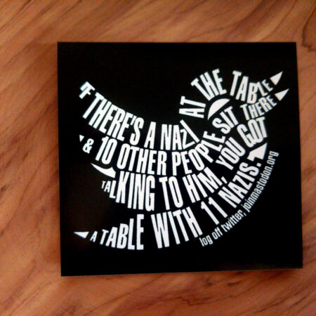 Woodgrain with a black square sticker laying on top. The black square contains a white bird (the twitter logo) made out of text that reads: "If there's a Nazi at the table & 10 other people sit there talking to him, you got a table with 11 Nazis." At the belly of the bird are the words, "log off twitter, joinmastodon.org"