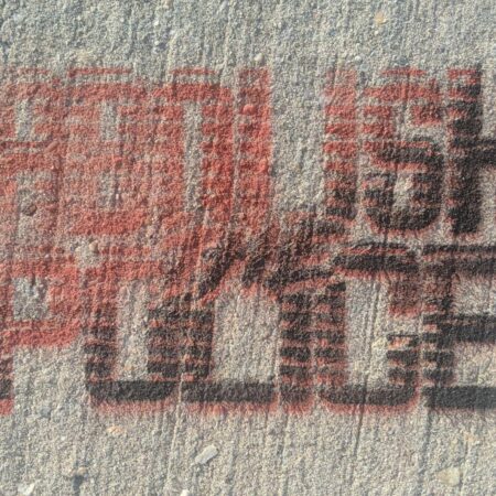 A rough concrete surface spraypainted through a stencil "Abolish the Police" in red and black ascending diagonal.